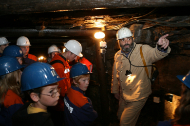 Bergmann erklärt Kindern in einem Besucherbergwerk etwas
