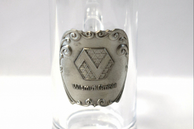 Schnapsglas mit Zinnrelief zeigt ein Logo 