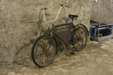 Gewöhnliches Fahrrad mit Rost und großem, weißen Lenker lehnt an der Wand des Anschauungsbergwerks im Deutschen Bergbau-Museum Bochum. Im Rahmendreieck ist ein rostendes Blechschild angebracht.