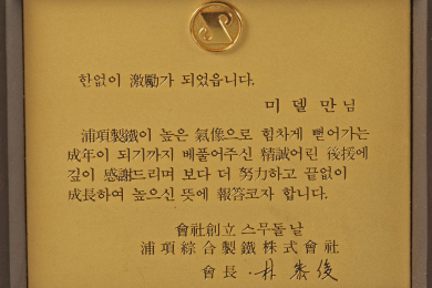 Zu sehen ist die Nahaufnahme einer goldfarbenen Metallplakette mit eingraviertem koreanischem Text. 