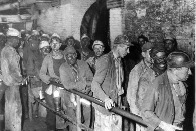 Das Foto zeigt etwa 20 Bergleute, die teilweise Lederkappen und teilweise Kopfschutzhelme „Barbara“ aus hellem Kunststoff tragen. Die Aufnahme ist vermutlich um 1958 entstanden, also in der Übergangszeit von der ledernen Kopfschutzkappe zum allgemein üblichen Kunststoffhelm in Bergwerken.