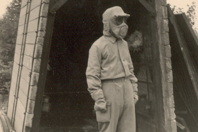 Ein Grubenwehrmann in Flammenschutzkleidung steht vor einem Versuchsaufbau bei der Hauptstelle für das Grubenrettungswesen des Ruhrbergbaus