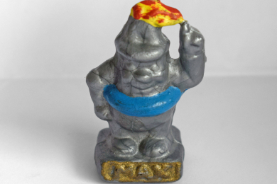 Kunststofffigur eines silbrigen Männchens mit spitzem Hut auf einem Sockel mit erhobenem linkem Arm, Flammen auf dem Kopf und einem blauen Schwimmreifen um den Bauch. Auf dem Sockel steht gold hervorgehoben MAX.