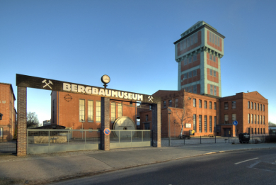 Eine Werkshalle mit Eingangstor und im Hintergrund ein gemauerter Förderturm