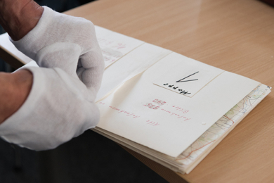 Ein Teilnehmer des Workshops mit weissen Handschuhen öffnet eine Karte aus dem Archiv