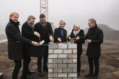 Fünf Personen stehen hinter einer für die Grundsteinlegung vorbereiteten kleinen Mauer.