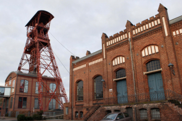 Ein rotes Fördergerüst aus Stahl neben einem Maschinenhaus