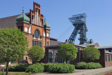 Ein historisches Zechengebäude mit einem Förderturm im Hintergrund