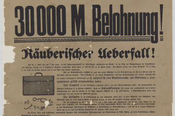 Ein Fahndungsplakat mit der Aufschrift „30.000 M. Belohnung! Räuberischer Überfall!“ mit der graphischen Darstellung einer Leder-Aktentasche und mehrerer Metallgegenstände wie Drahtseil, Schraubzwingen, Haken. 