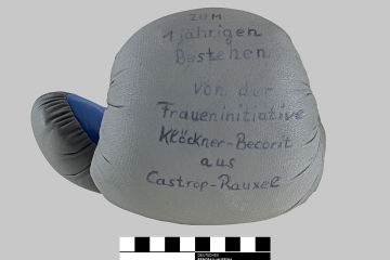 Frontansicht eines blaugrauen Boxhandschuhs mit Filzstift-Aufschrift: „Zum 1-jährigen Bestehen von der Fraueninitiative Klöckner-Becorit aus Castrop-Rauxel“
