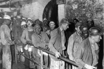 Das Foto zeigt etwa 20 Bergleute, die teilweise Lederkappen und teilweise Kopfschutzhelme „Barbara“ aus hellem Kunststoff tragen. Die Aufnahme ist vermutlich um 1958 entstanden, also in der Übergangszeit von der ledernen Kopfschutzkappe zum allgemein üblichen Kunststoffhelm in Bergwerken.