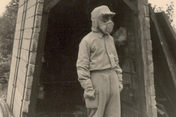 Ein Grubenwehrmann in Flammenschutzkleidung steht vor einem Versuchsaufbau bei der Hauptstelle für das Grubenrettungswesen des Ruhrbergbaus