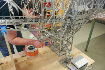 Ein Mann lötet in der Werkstatt des Deutschen Bergbau-Museums Bochum ein Teil eines Modells einer großen technischen Vorrichtung im Bergbau zum Transport von Fördergut über den offenen Tagebau hinweg.