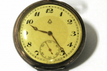 Ziffernblatt einer Taschenuhr unter gelben Uhrglas 