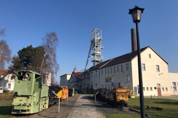 Das Fördergerüst mit Betriebsgebäude und historischen Grubenbahnen