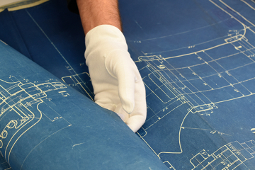 Ein Museumsmitarbeiter mit weissen Handschuhen faltet vorsichtig einen historsichen Plan auseinander