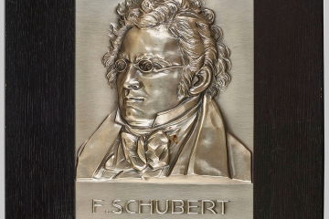 Metallrelief in einem breiten Holzrahmen, das ein Porträt des Komponisten Franz Schubert zeigt