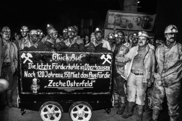 Förderwagen mit der Aufschrift  Die letzte Förderkohle in Oberhausen vor einer Gruppe von Bergleuten in Arbeitskleidung