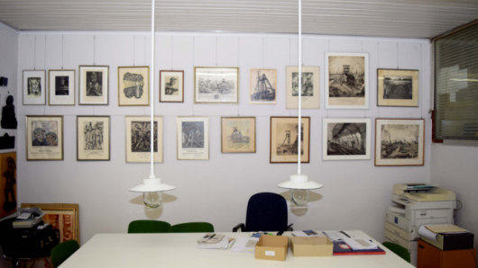 Eine Stellwand hinter einem Arbeitstisch zeigt Bilder von Zechen.