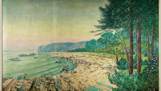 Zu sehen ist eine Küstenlandschaft. Links das Meer, vorne und mittig der Strand mit Gesteinen, rechts Bäume und blühende Pflanzen, im Hintergrund aufragende Felsen.